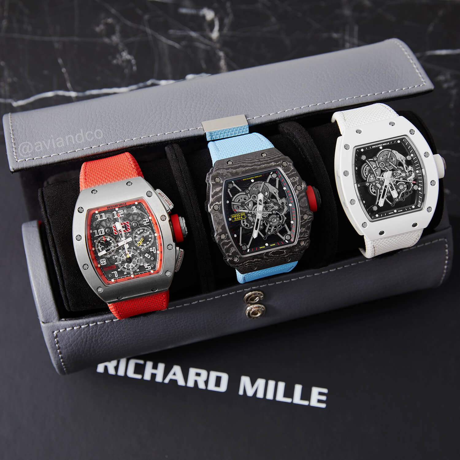 Stainless Steel Bezel with Red Strap, Carbon Bezel with Light Blue Strap, and White Bezel and Strap all in a Black Leather Watch Roll on a Black Background