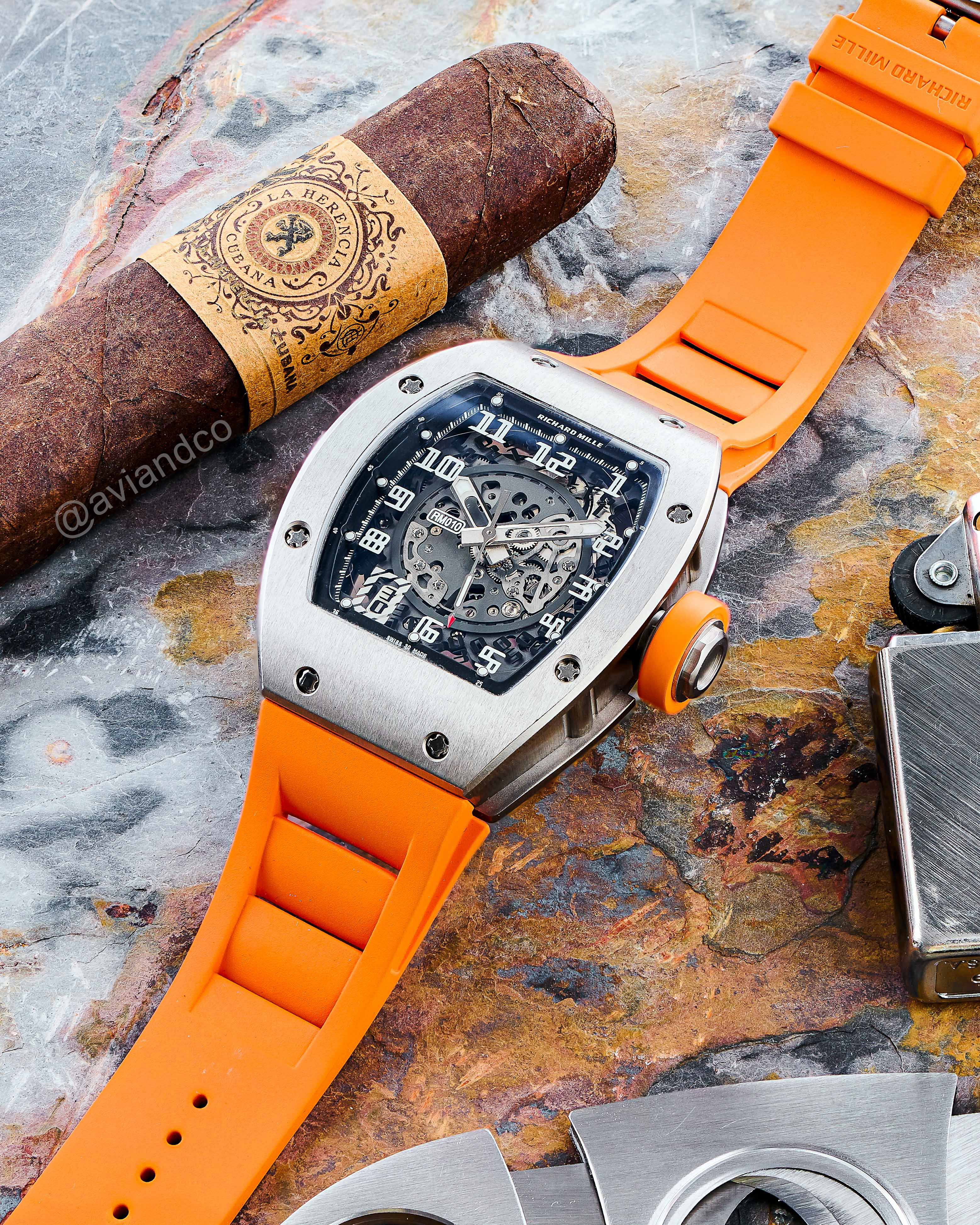Stainless Steel Bezel with Skeleton Dial and Neon Orange Rubber Strap on a Marble Tabletop Surrounded by a Cuban Cigar, Lighter, and Cutter