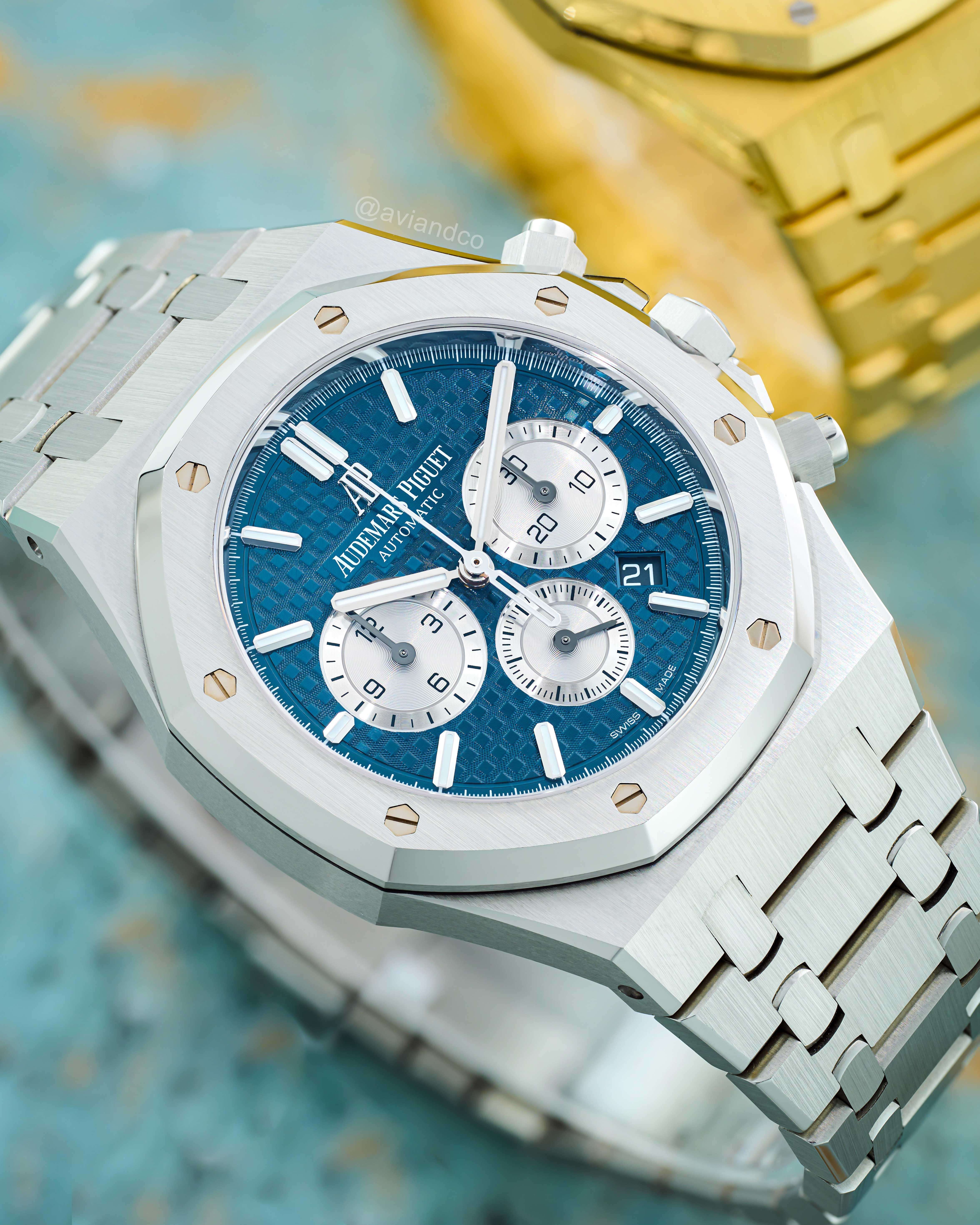 Stainless Steel Chronograph with Blue Index Dial Wrapped Around a C-Ring with Light Blue Marble Background.