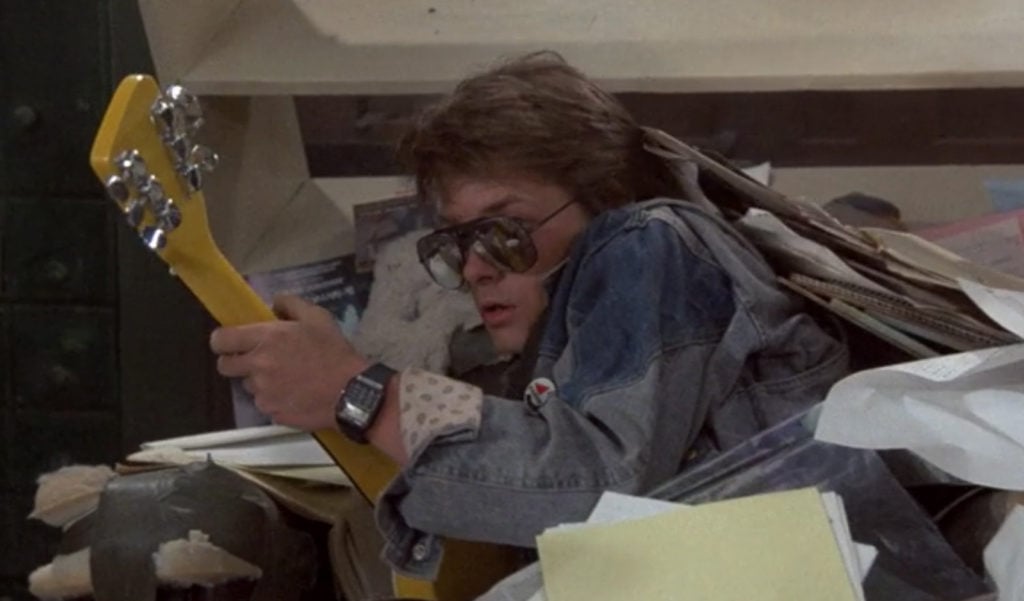 Movie Still from Back to the Future of Michael J. Fox Holding a Yellow Guitar After Falling into a Stack of Papers