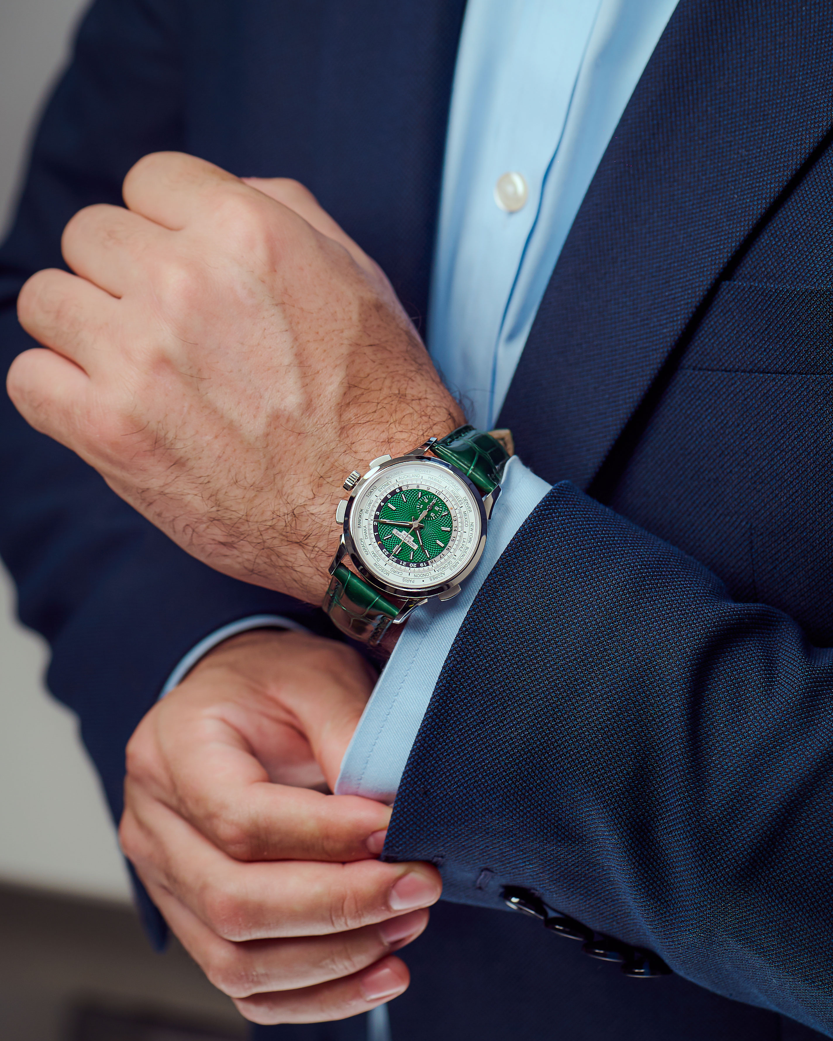 Platinum Timepiece with Green Index Dial and Green Leather Bracelet on the Wrist of a Man with Navy Blue Jacket and Light Blue Button Down