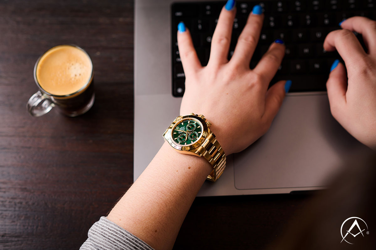 18K Yellow Gold, Green Dial Timepiece on a Ladies Wrist Typing on a Laptop Beside an Espresso