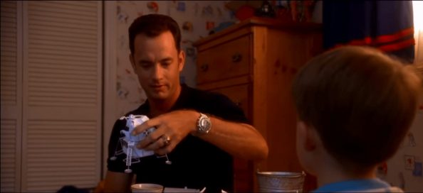 Movie Still from Apollo 13 of Tom Hank’s Character Holding a NASA Toy While Talking to His Son and Sporting a Stainless Steel Timepiece