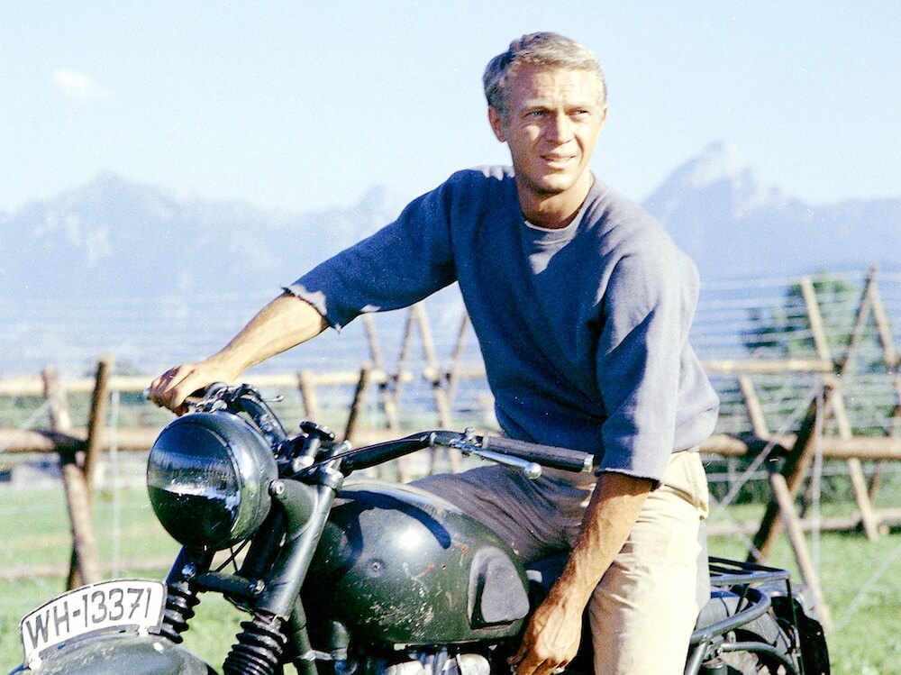 Academy Award Nominee Steve McQueen sits on a Rusty Motorcycle in a Field from the Film The Great Escape
