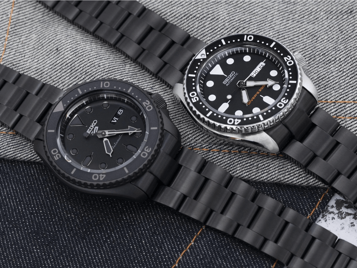 Two Timepieces, Both Black, Lay Flat on a Dark Jean Background