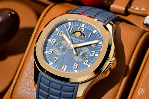 Patek Philippe Aquanaut watch with gold bezel, blue dial, and blue rubber strap pictured on cognac leather background