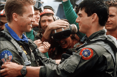 Movie Still from Top Gun of Tom Cruise Sporting a Chronograph with Fellow Actor Wearing Pilot Uniforms with Men Behind Cheering Behind Them