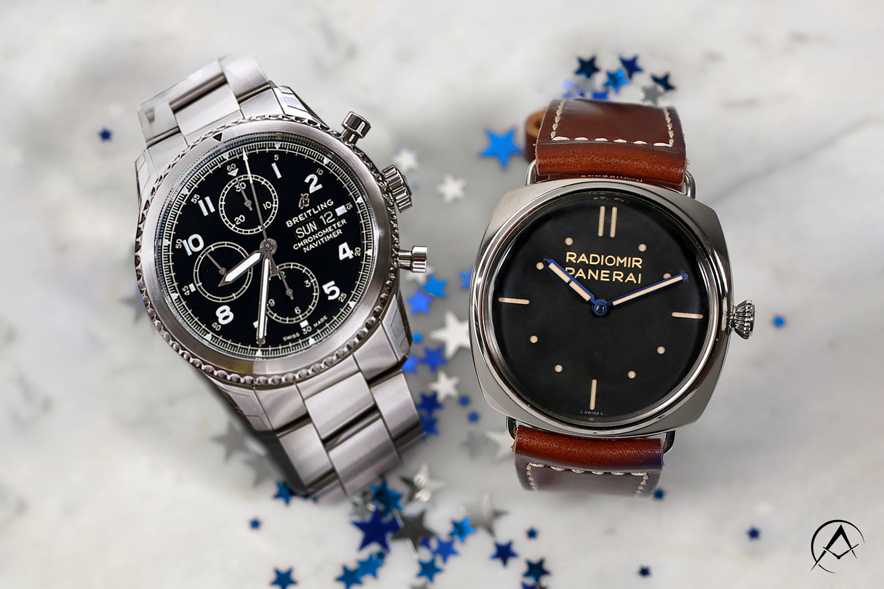 A Sterling Silver Breitling with Black Dial Sits Beside a Sterling Silver Panerai Radiomir with Brown Leather Strap on a White Marble Tabletop with Blue and Silver Stars.