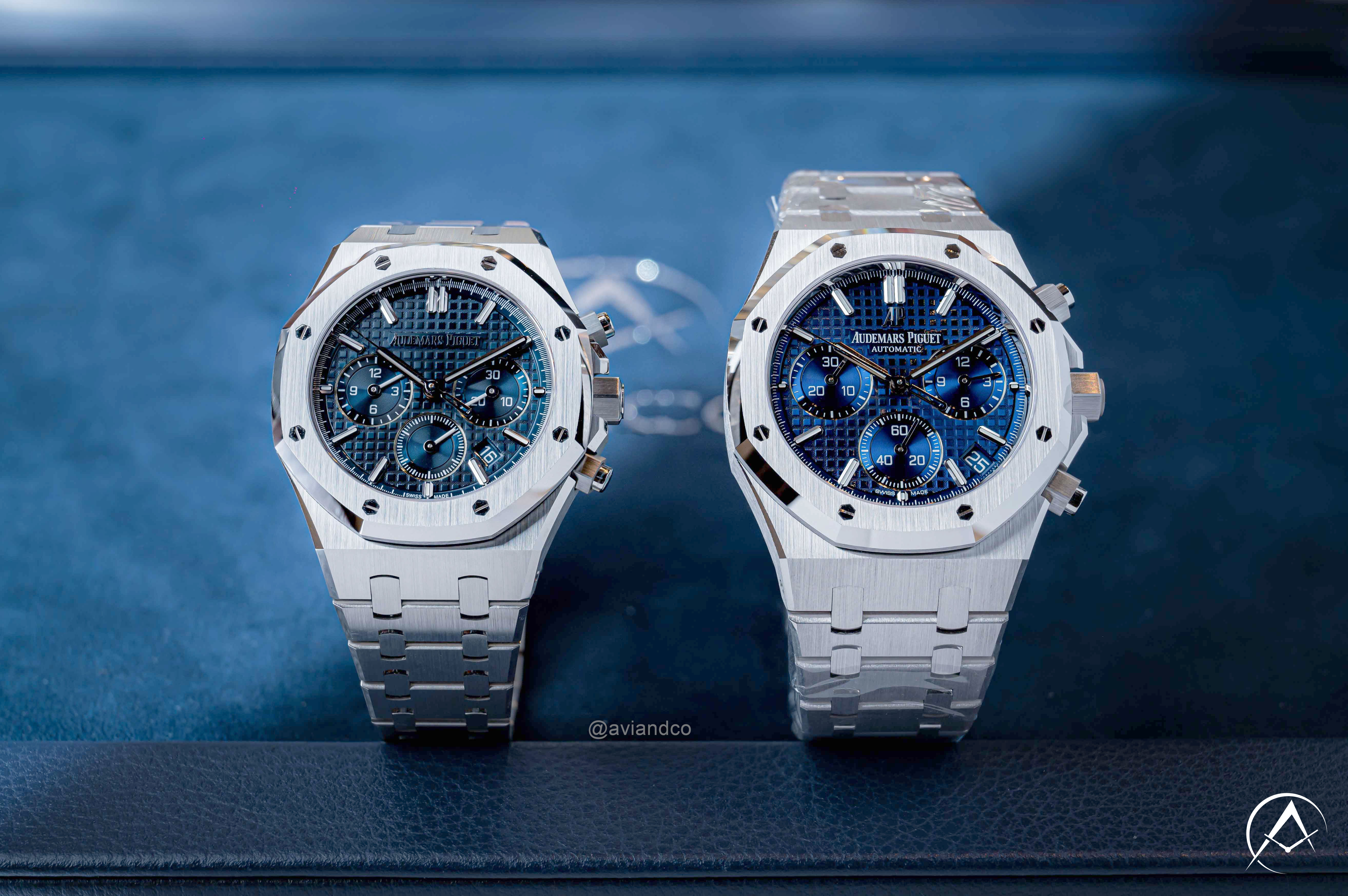 Stainless Steel and 18K White Gold 41 mm Audemars Piguet Royal Oak Chronograph Luxury Timepieces with Blue Dials Displayed on Clear C-Rings Above a Navy Blue Avi & Co. Watch Pad.