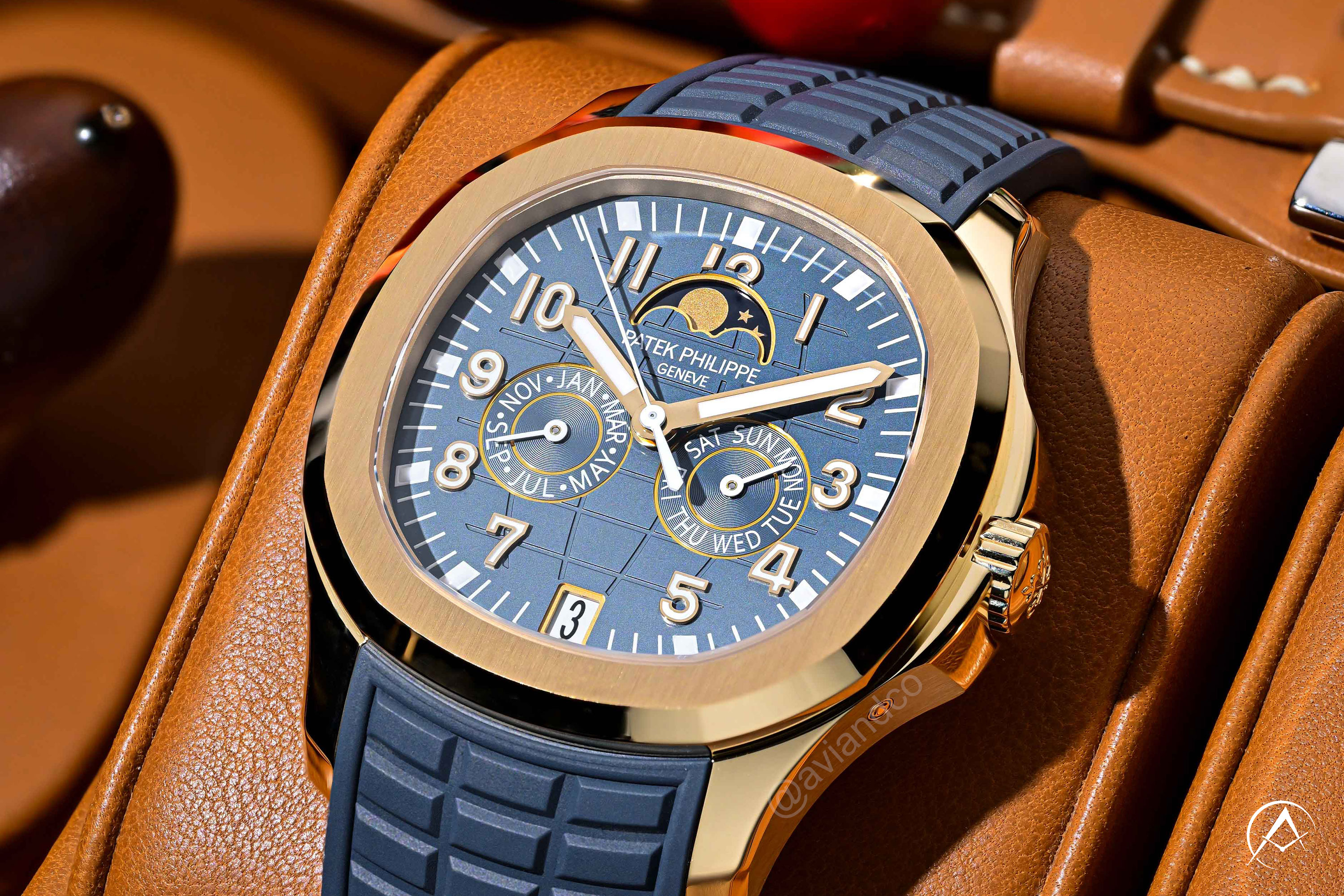 Patek Philippe Aquanaut watch with gold bezel, blue dial, and blue rubber strap pictured on cognac leather background