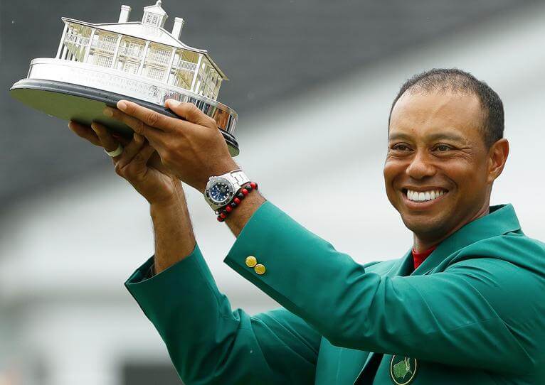 Man Wearing Green Blazer Holds a Golf Award While Wearing Rolex Timepiece Around his Wrist.