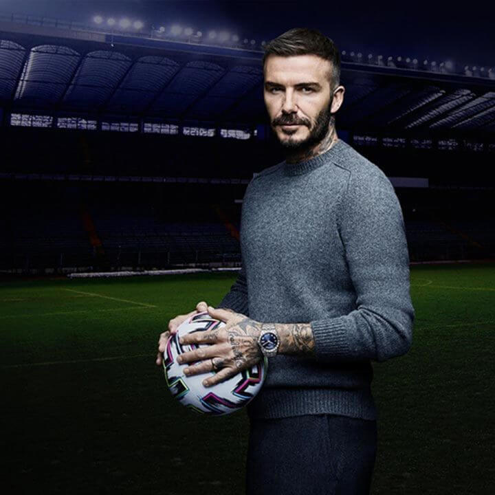 Professional Soccer Player Stands in Stadium Holding a Soccer Ball and Wearing a Tudor Timepiece Around his Wrist.