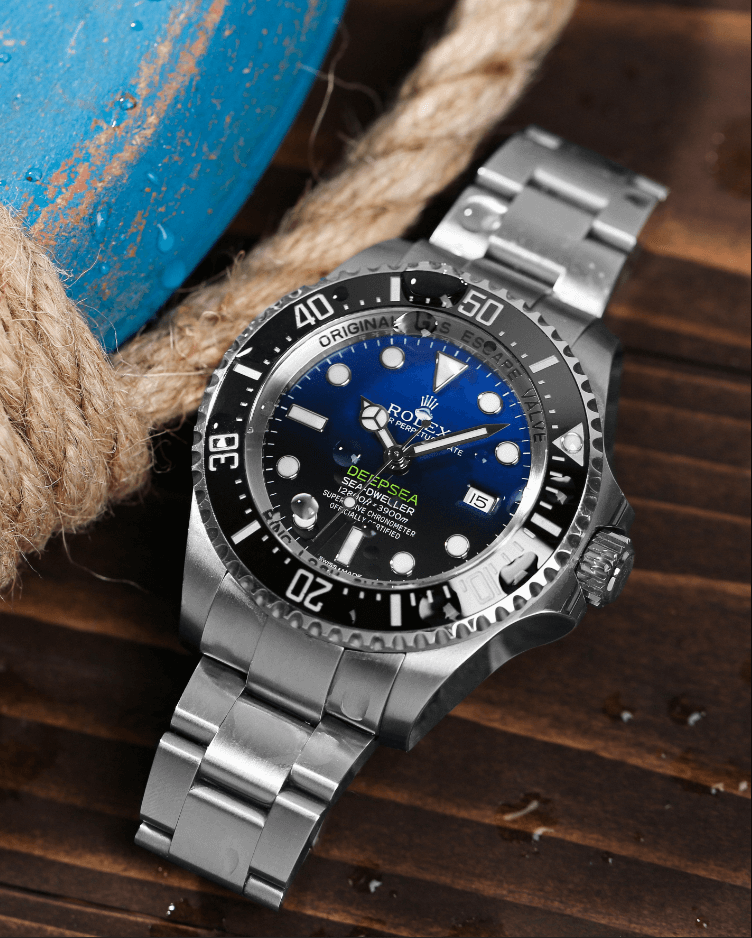 Black and Blue Dial with Black Bezel Timepiece on a Stainless Steel Bracelet, Lying on a Wooden Table.