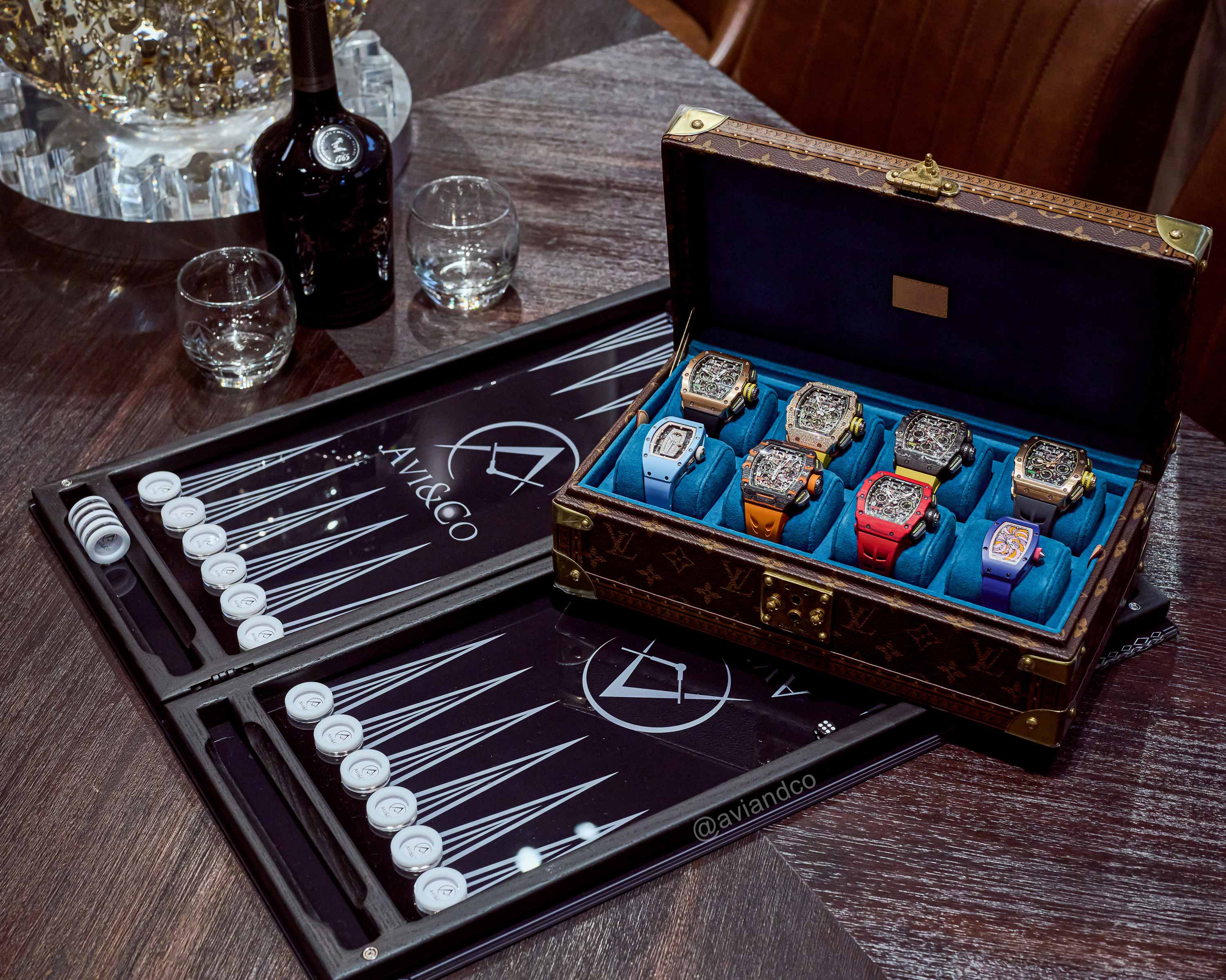 Eight Richard Mille Luxury Timepieces in a Brown Watch Case Displayed on Top of an Avi & Co. Backgammon Game on a Brown Table.