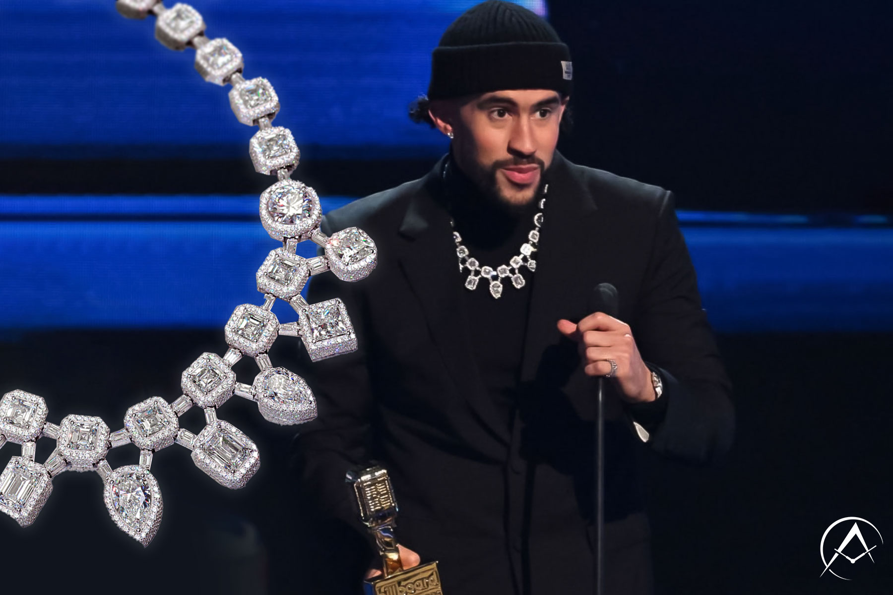 Man Stands on Stage Holding Latin Music Award While Wearing Black Suit with Black Turtleneck and Beanie, and Diamond-Pave Chain.