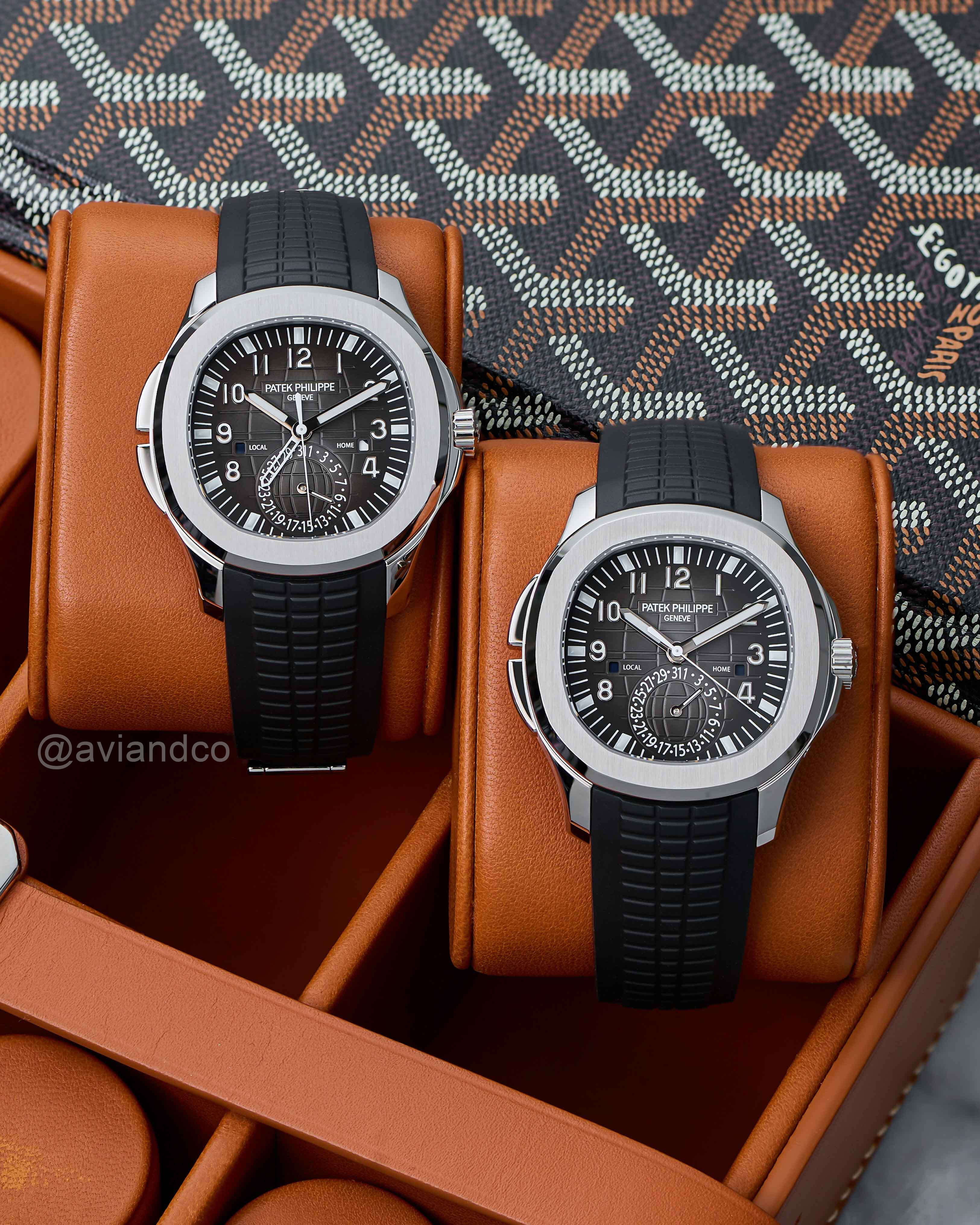 Two Identical Stainless Steel Timepieces with Dual Time Zones, Black Dials, and Black Rubber Bracelets Displayed on Brown Watch Cushions.