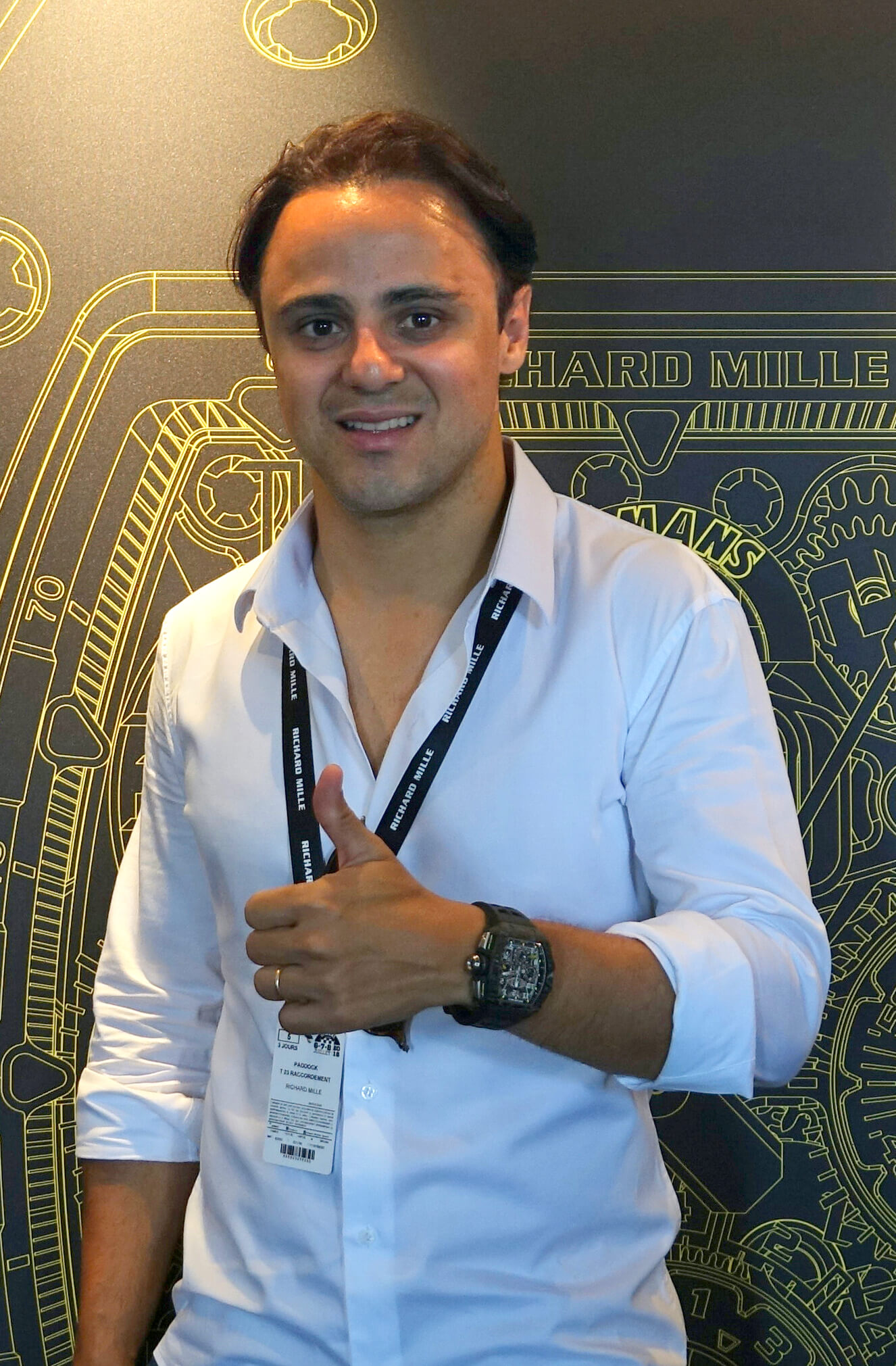Man Wearing Black Richard Mille Timepiece and a White Button-down Shirt Smiles in Front of a Richard Mille Schematic.
