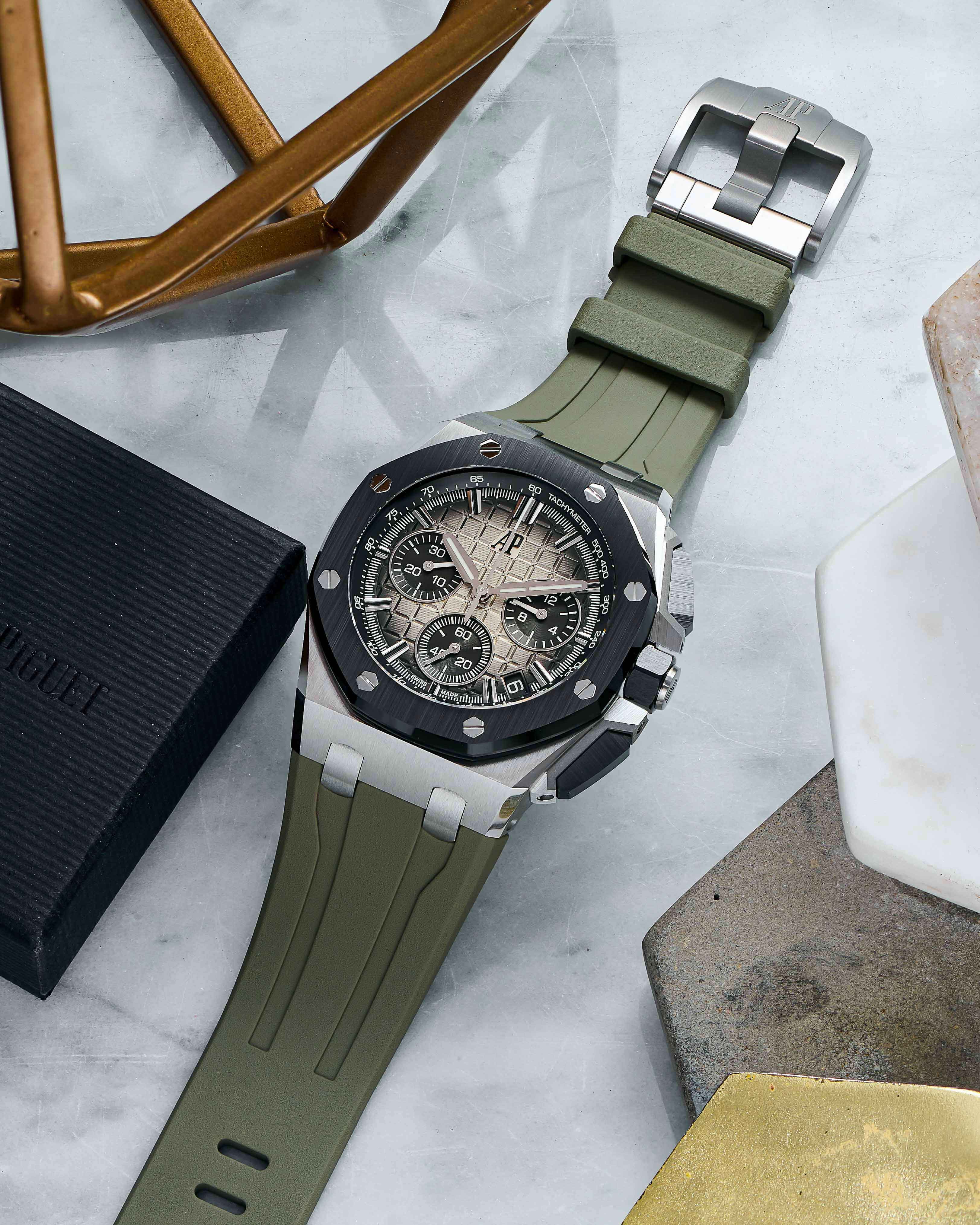 A Black Bezel Timepiece on a Rubber Green Strap Lays Across a Marble Tabletop.