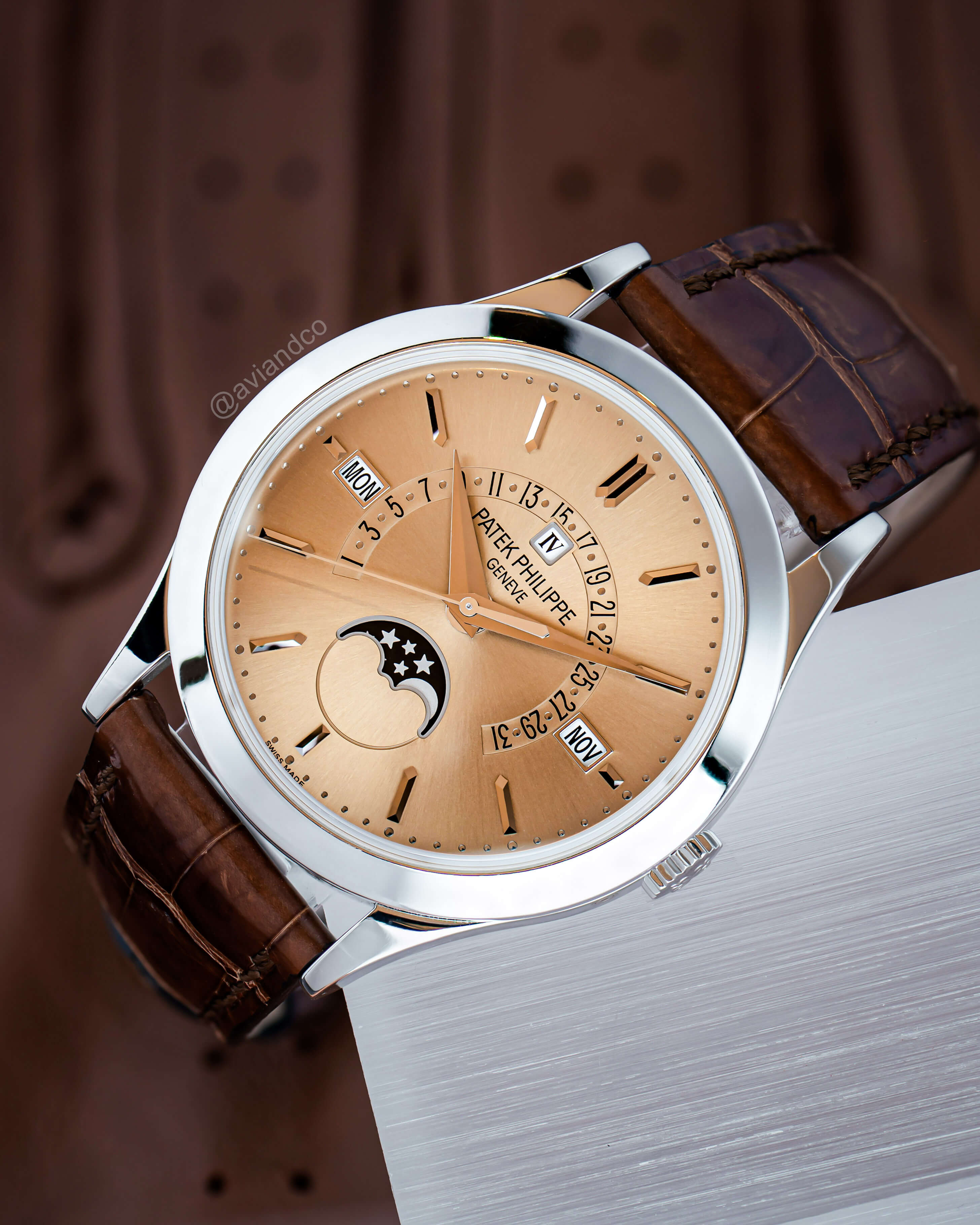 Platinum Timepiece with Perpetual Calendar, Brown Index Dial, Brown Leather Bracelet Displayed on a C-Ring on a Brown Leather Background.