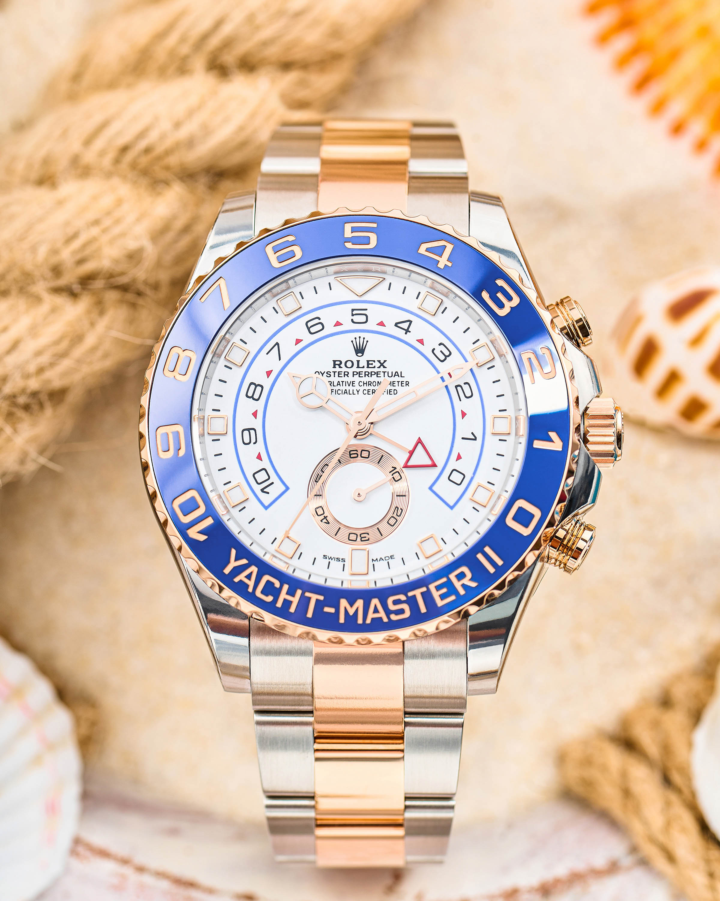 18K Yellow Gold Rolex Yacht-Master II Timepiece with White Dial on a Nautical Background with Ropes and Seashells.