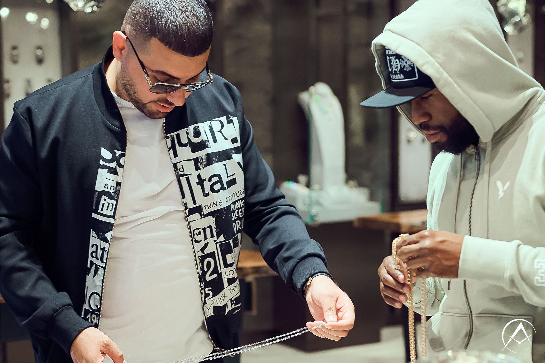 Two Men in Trendy, Upscale Boutique with Luxury Watches such as Patek Philippe and Rolex in Glass Cases Looking at Custom Diamond Jewelry.