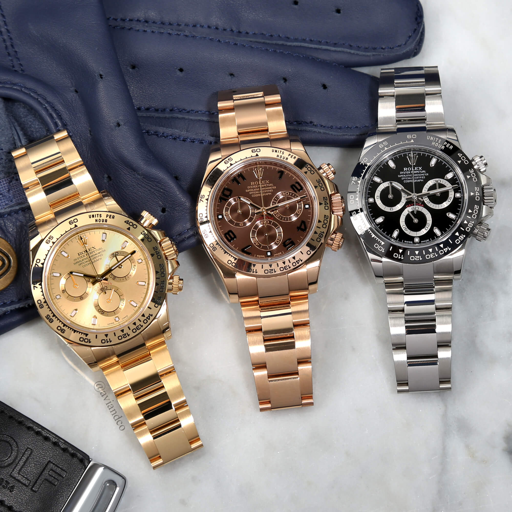 Three Rolex Cosmograph Daytona Timepieces Lying on a White Marble Tabletop with a Blue Glove.