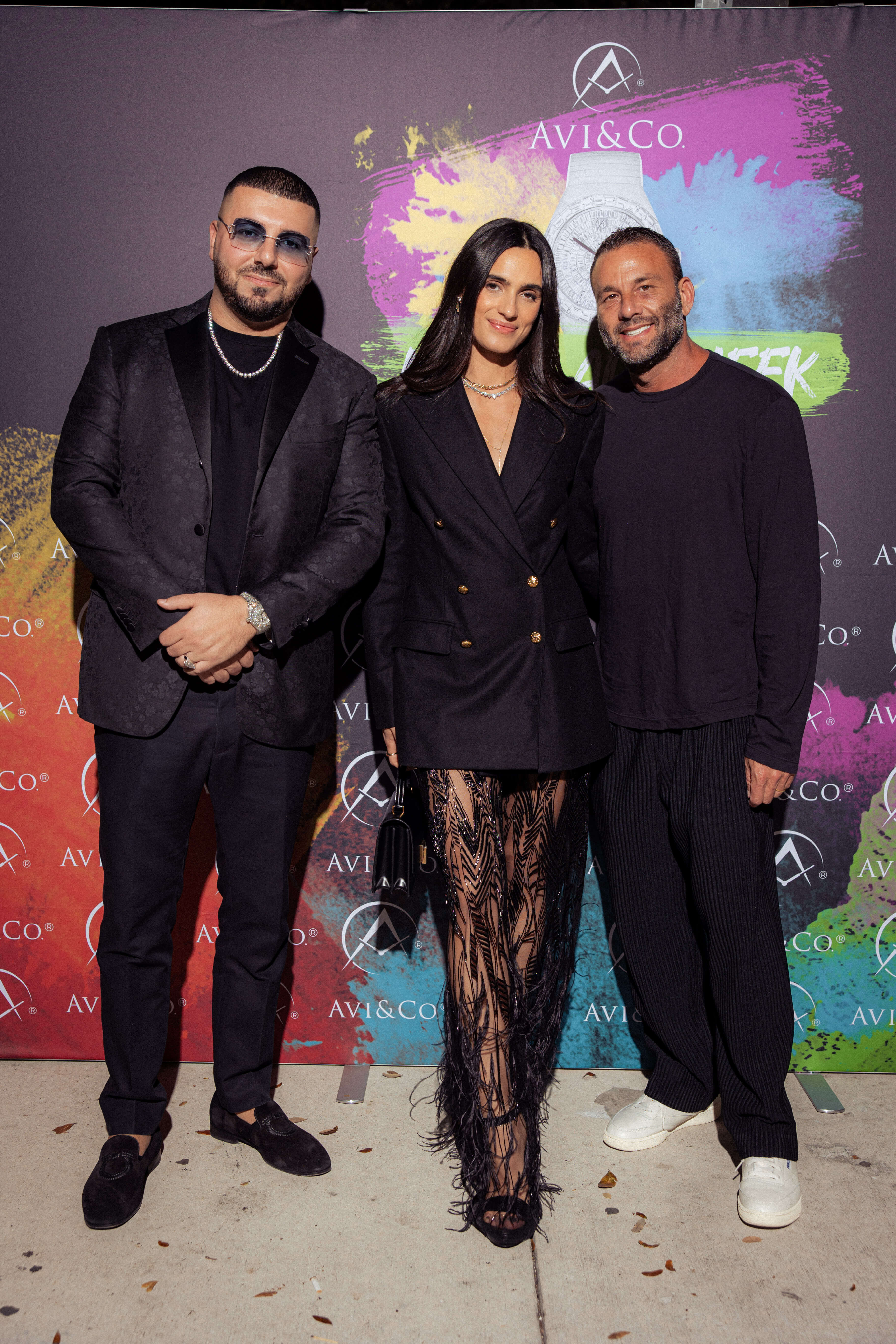 Two Men and One Woman Wearing All Black in Front of Avi & Co.'s Miami Boutique Step and Repeat Celebrating the Launch of Isa Grutman Jewelry.