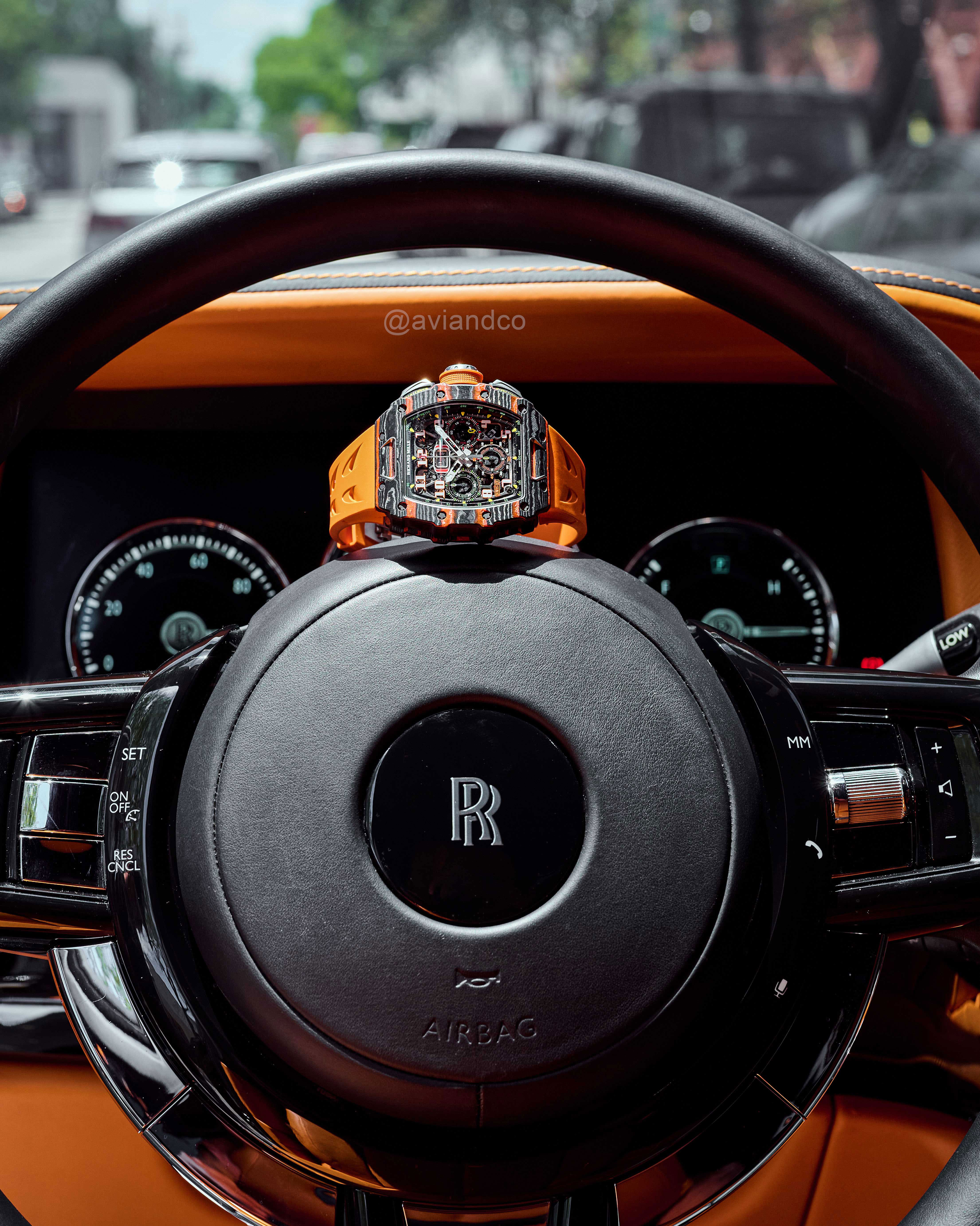 Carbon 44 mm Timepiece Assembled with Quartz TPT Bezel and Orange Rubber Strap Sitting on Top of a Steering Wheel Inside a Black and Orange Car.