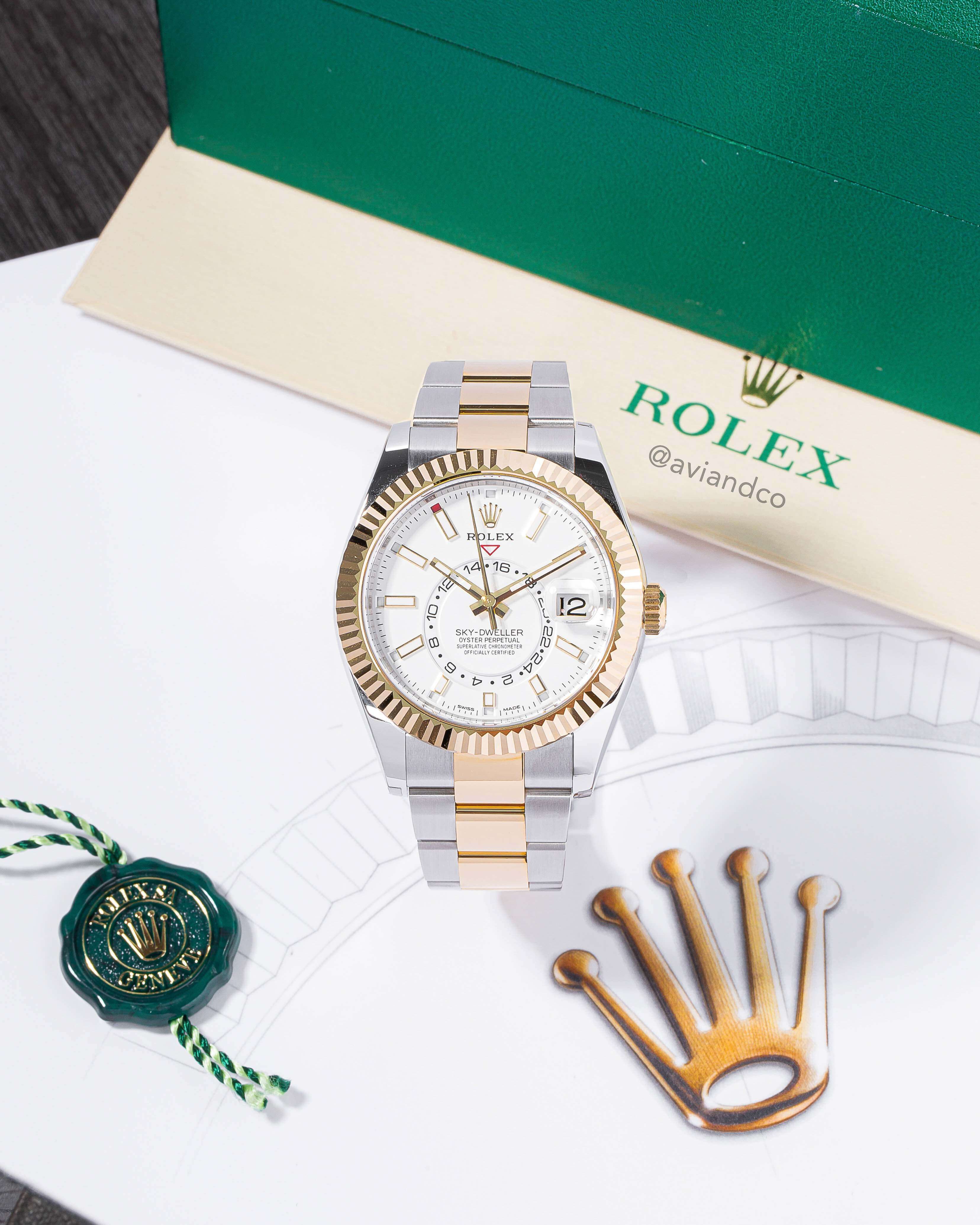 This Stainless Steel and 18K White Gold 42 mm White Dial with Yellow Gold Bezel Timepiece has an Automatic Movement and is Displayed on a C-Ring on a Rolex Background.