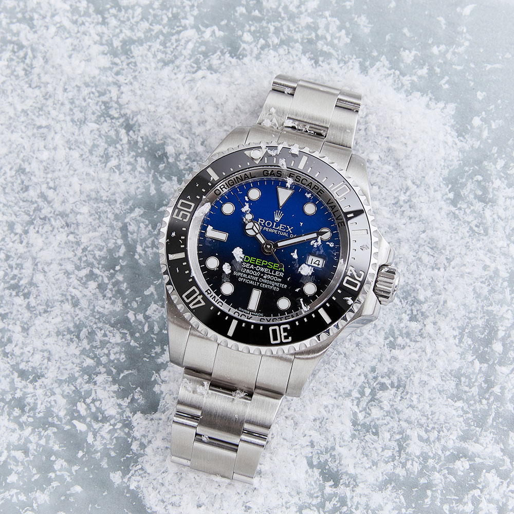 Deepsea Blue Dial Timepiece with Black Ceramic Bezel and Stainless Steel Oyster Bracelet on a White Snowy Background.