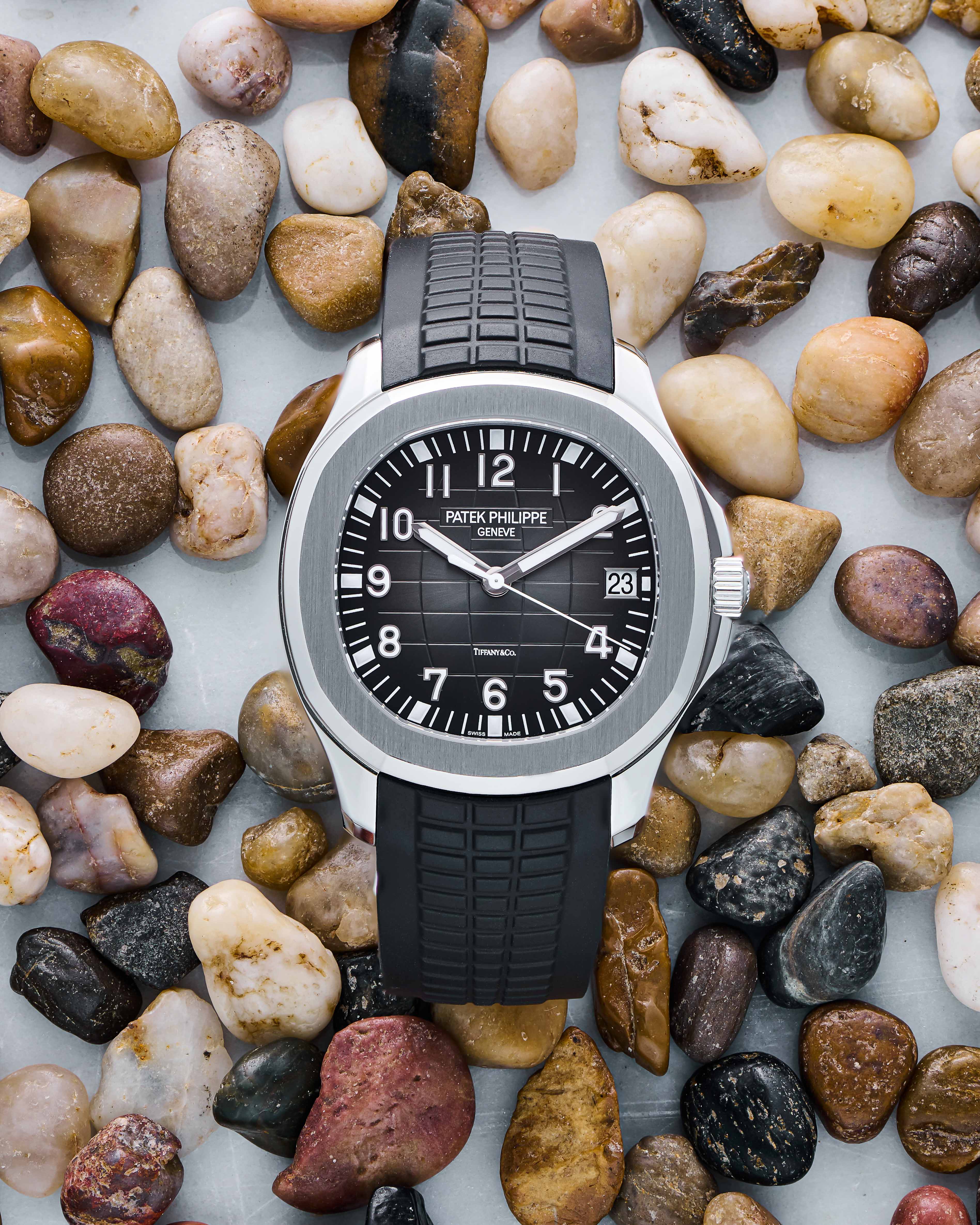 Luxury Timepiece with Black Arabic Dial, Black Rubber Bracelet, Date Function, and Fixed Bezel on a Rock Background.
