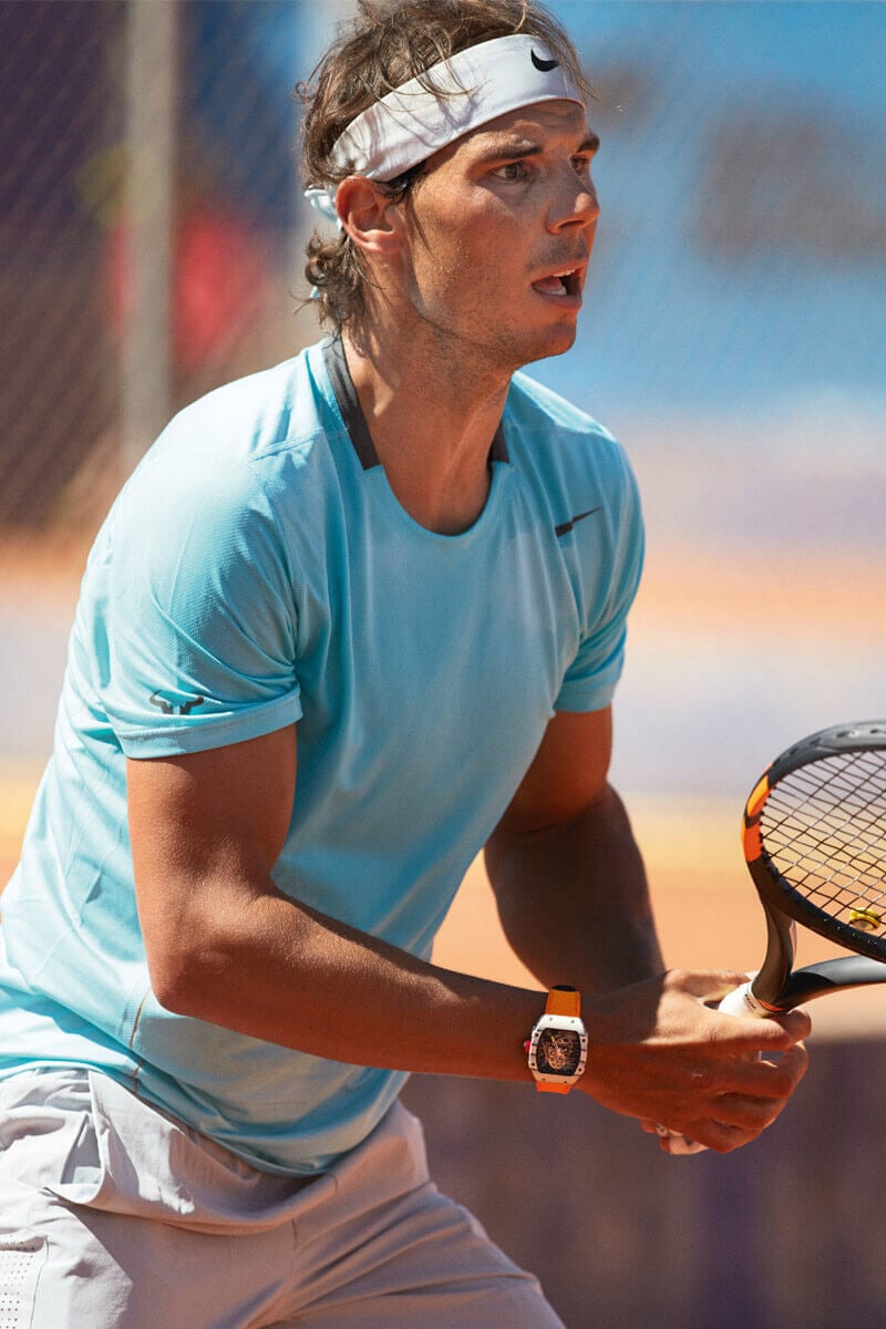 Professional Tennis Player Holding a Tennis Racket, Wearing an Orange Richard Mille Timepiece Around his Wrist.