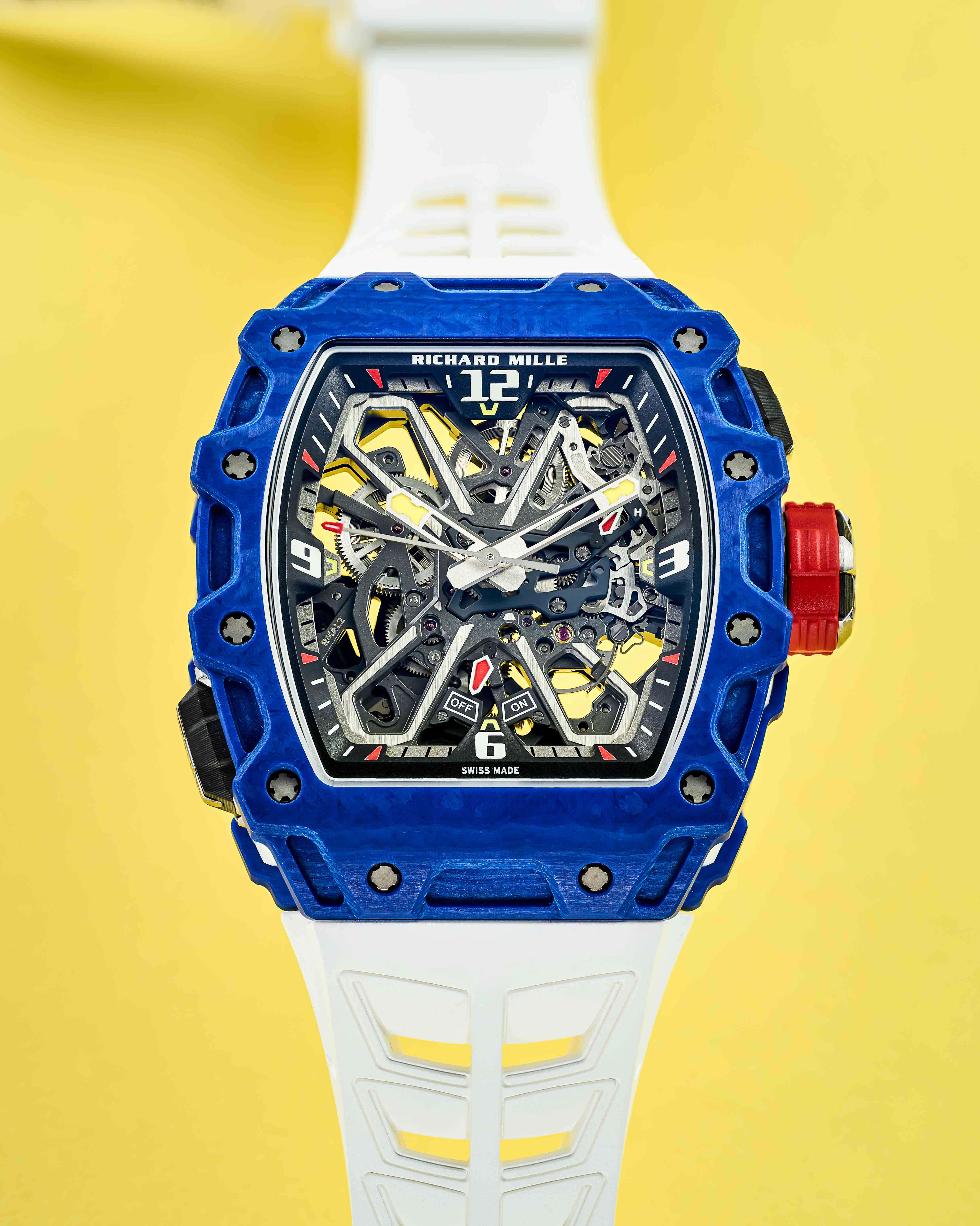 Blue Bezel Timepiece with Openworked Dial, Red Crown, and White Rubber Strap on a Yellow Background.