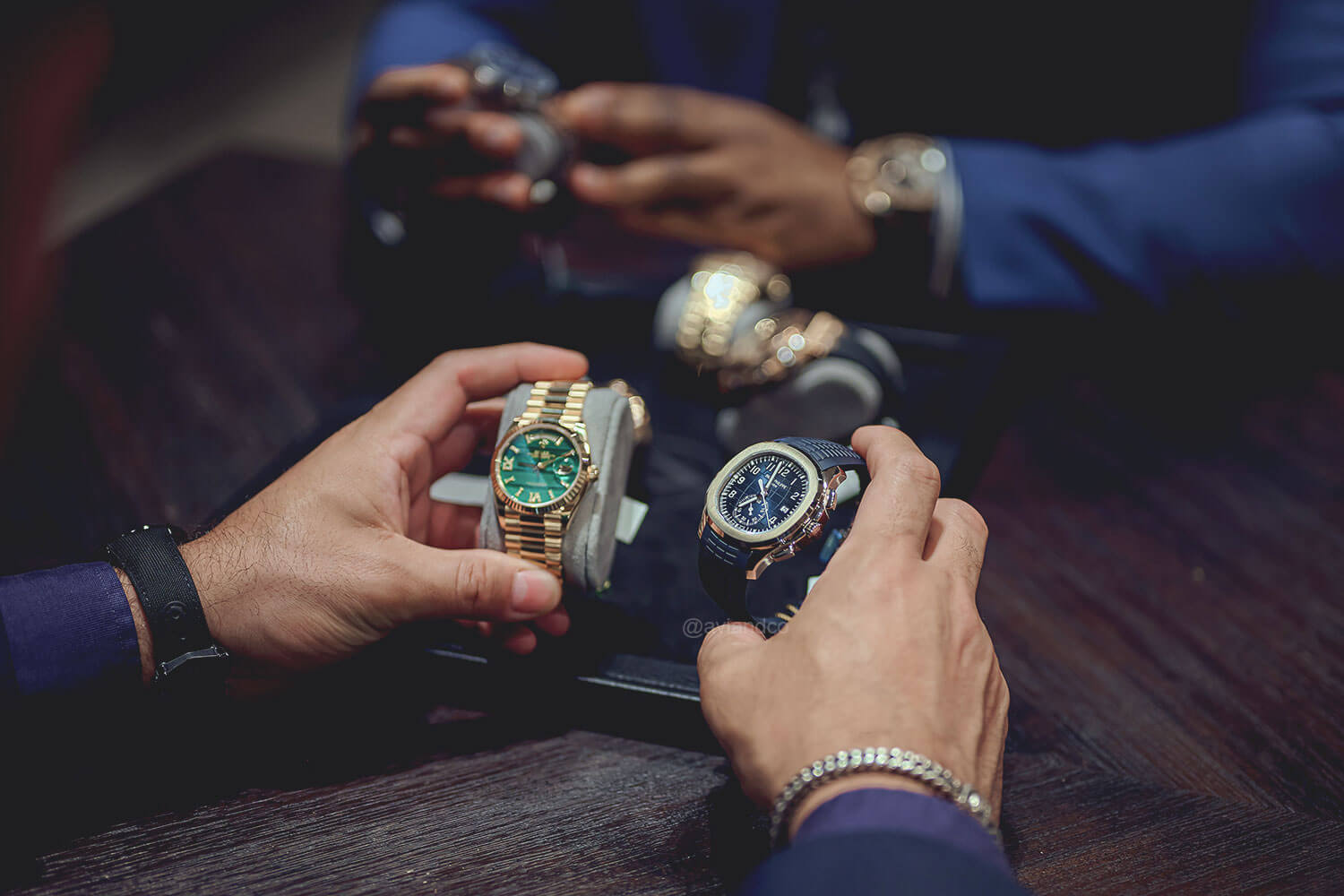Man Holds a Rolex with Green Dial and Patek Philippe with Blue Dial in Front of Another Man with Additional Watches to Choose From.