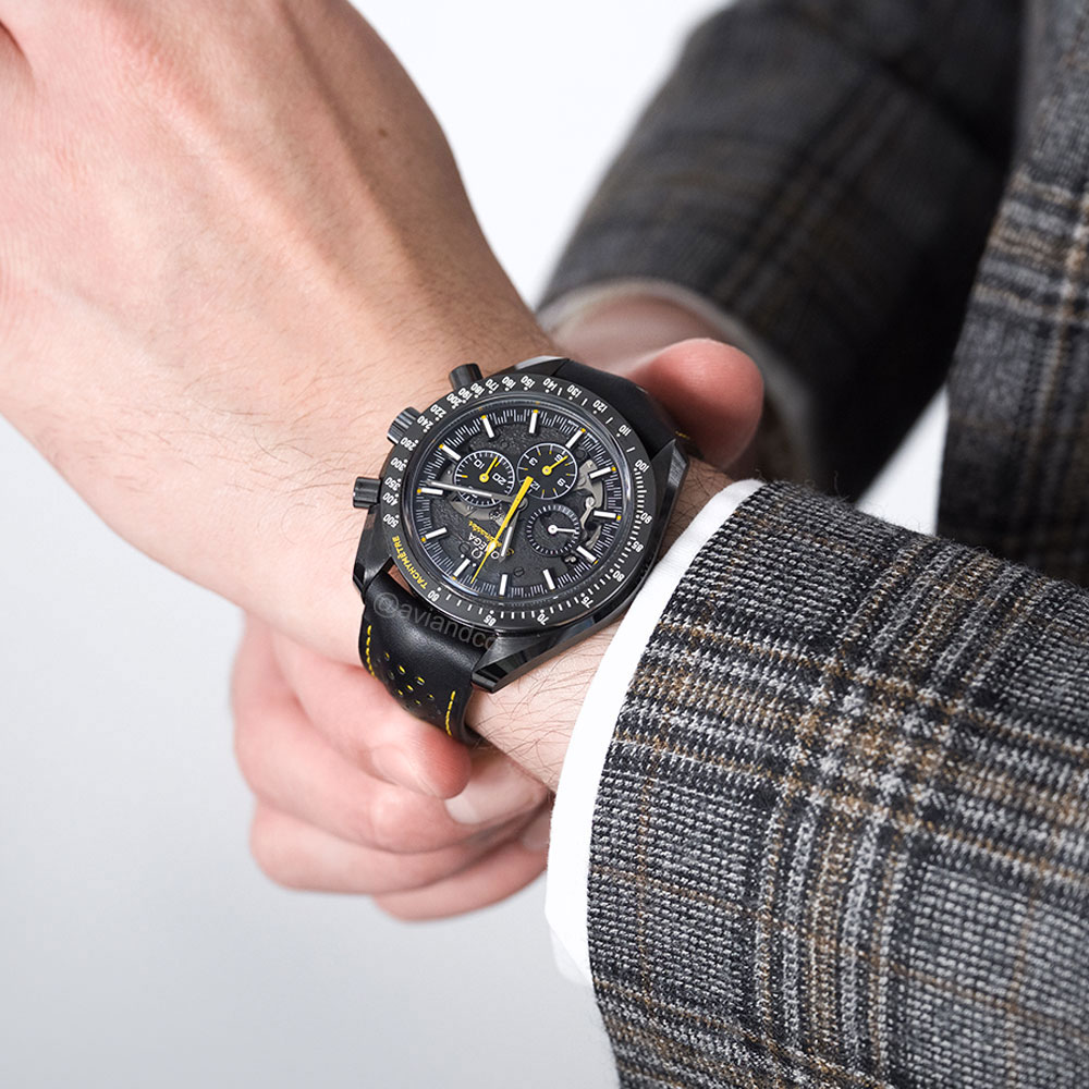 Omega Speedmaster watch on wrist with black band and face, yellow accents